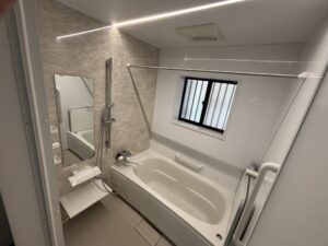 完成した浴室全景。白とベージュ系の壁パネル、LED照明、鏡、手すりが整然と配置され、明るく清潔な空間に仕上がっている