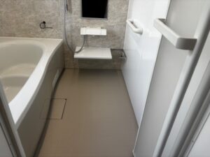 完成した浴室の全景。白色の浴槽とグレー系石目調の壁パネル、ベージュ系の床が調和している。シャワー水栓・収納棚・タオル掛けが機能的に配置され、清潔感のある仕上がり
