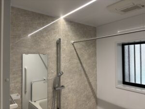 浴室壁面とシャワー設備のアップ。ベージュ系のアクセント壁、スライドバー付きシャワー、LED照明が機能的に配置されている