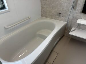 浴槽と手すりの詳細。白色の浴槽エプロンに手すりが取り付けられ、安全性に配慮されている。壁はグレー系石目調パネル、床はベージュ系の樹脂製で水はけの良い形状