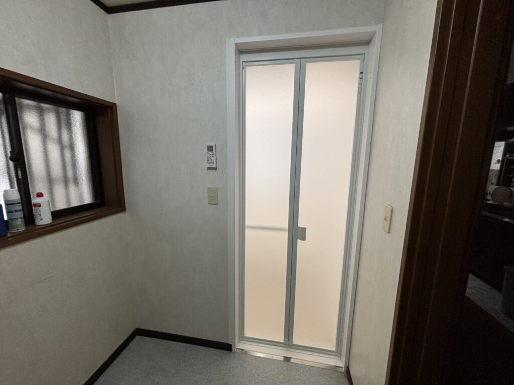 完成した浴室入口。内窓が取り付けられた引き戸が設置され、白い枠と半透明ガラスで明るく開放的な印象を与えている