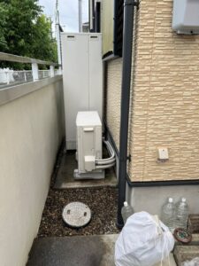 設置スペース全景。新しいエコキュート室外機が手前に配置され、配管は壁面に沿って整然と這わせてある