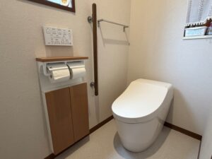 完成した1階トイレ。TOTO GGA3（アイボリー）が設置され、左壁に木目調の埋め込み収納と手すり、壁面スイッチパネルが並びます