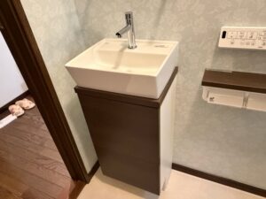 手洗い器まわりの完成。LIXIL キャパシアの白い陶器ボウルとダークブラウンの収納キャビネットが組み合わされています