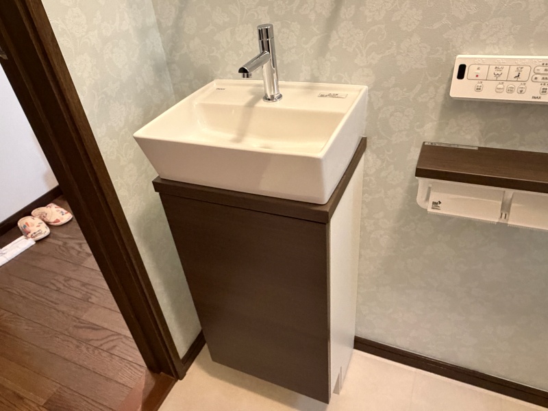 手洗い器まわりの完成。LIXIL キャパシアの白い陶器ボウルとダークブラウンの収納キャビネットが組み合わされています