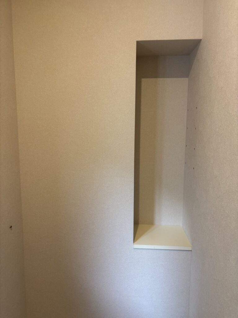 1階トイレの埋め込み収納ニッチ。白い内装で仕上げられ、奥行きのある棚板が水平に取り付けられています